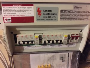 A picture showing a new electrical installation of a Consumer Unit by London Electricians, with a warning sign saying that it needs frequent electrical testing