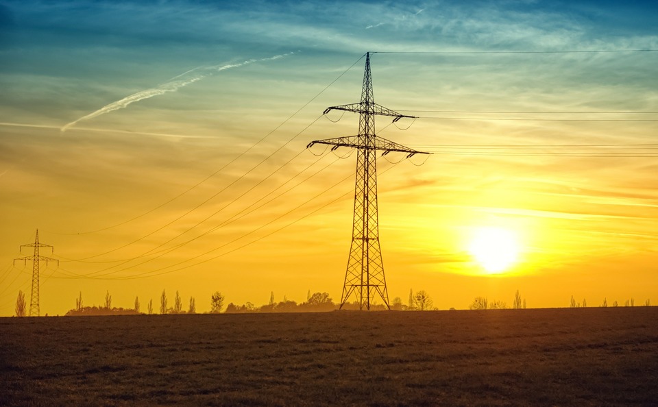 An image of a large electricity transmission tower with the sun setting behind it.